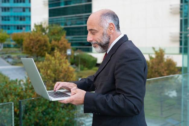 Free photo side of positive mature business leader working with laptop