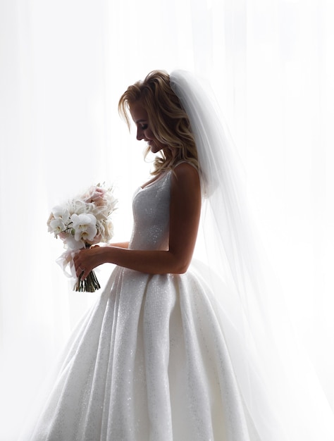 Side view of  adorable fiancee, wearing in wedding sparkle dress and veil, considering flowers