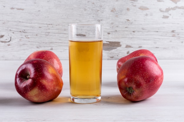 Free photo side view apple juice with red apples on white wooden table