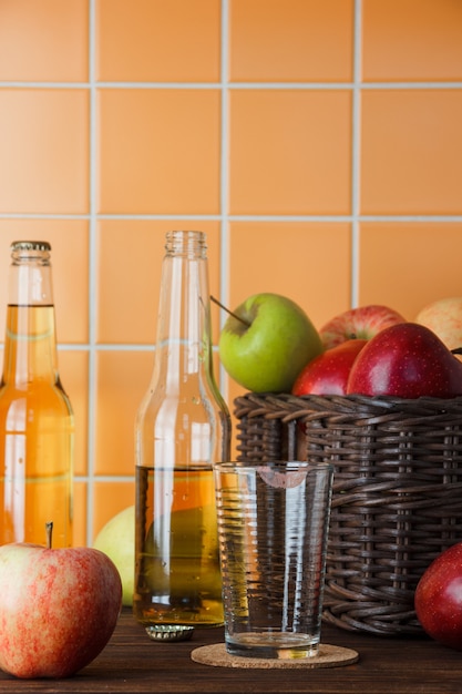 Side view apples in basket with apple juice on wooden and orange tile background. vertical space for text