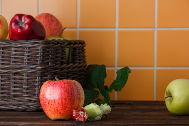 Side view apples in basket with bitten one on wooden and orange tile background. horizontal