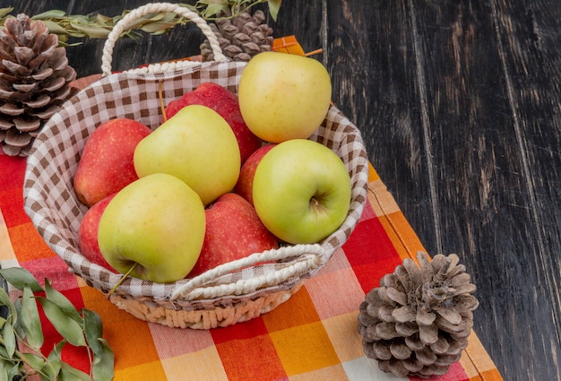 Free Photo side view of apples in basket with pinecones on plaid cloth and wooden