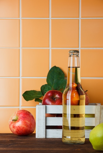 Side view apples with apple juice in a box on wooden and orange tile background. vertical space for text