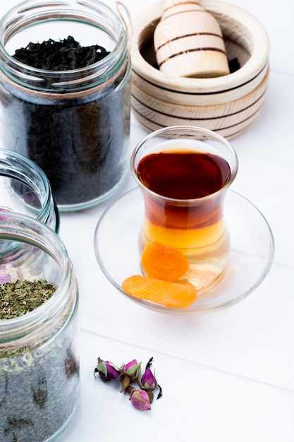 Free Photo side view of armudu glass of tea with various spices and herbs in glass jars on white