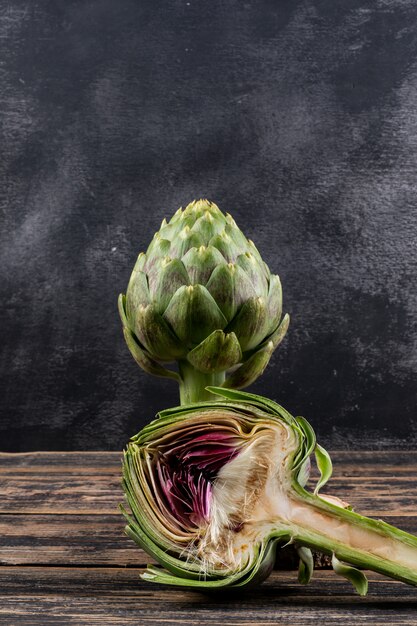 Free Photo side view artichoke and a slice on dark wooden and black background. horizontal space for text