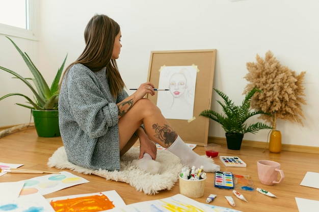 Free Photo side view artist sitting on the floor and painting on canvas