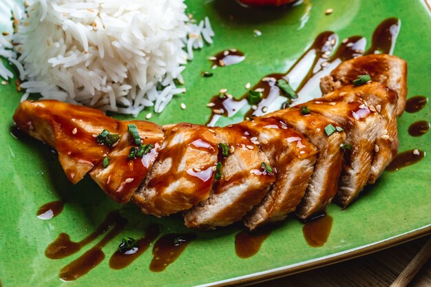 Side view baked chicken breast with spring onion sauce sesame seeds and rice on a plate