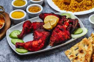 Free photo side view baked chicken with cucumber lemon seasoning and bread on the table