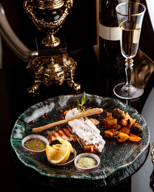 Free Photo side view of baked fish fillet  garnished with vegetables   spices and sauce on a plate   with a glass of white wine on the table