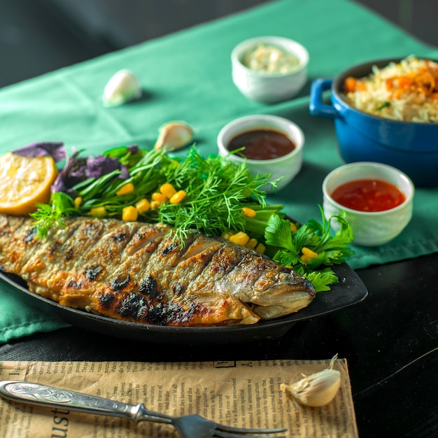 Side view of baked sea bass served with fresh herbs and sauces on the table