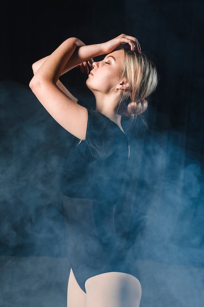 Free Photo side view of ballerina posing with arms in smoke