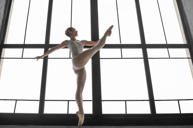 Side view of ballerina stretching by the window