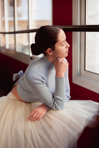 Side view of ballerina in tutu skirt looking through the window