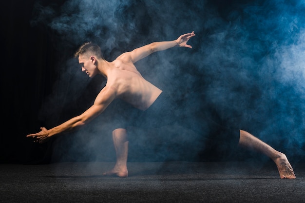 Free photo side view of ballerino posing in smoke