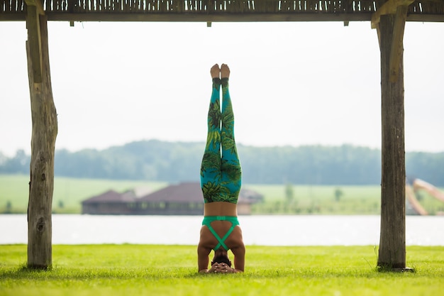 Side view of barefoot young concentrated woman doing handstand in park in summer day