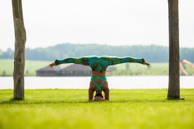 Side view of barefoot young concentrated woman doing handstand in park in summer day