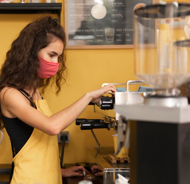 Side view barista wearing a medical mask while making coffee indoors