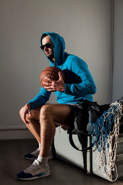 Free photo side view of basketball player posing in hoodie with ball