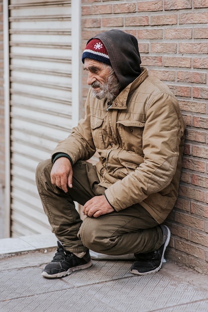 Side view of bearded homeless man in front of brick wall