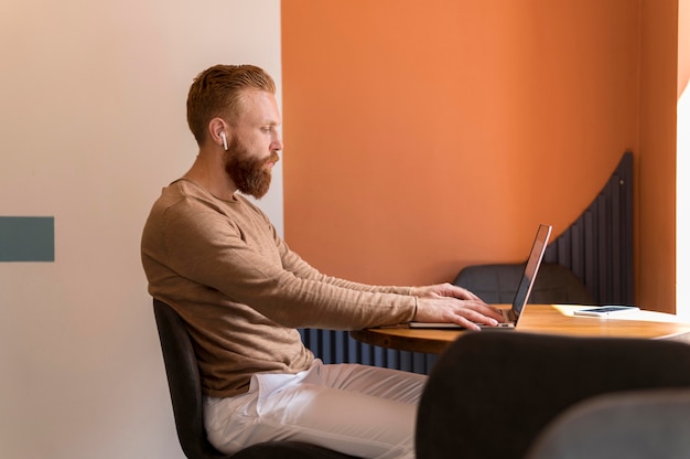 Free photo side view bearded man working on laptop