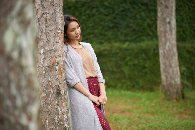 Side view of beautiful woman leaning the tree and looking away from camera