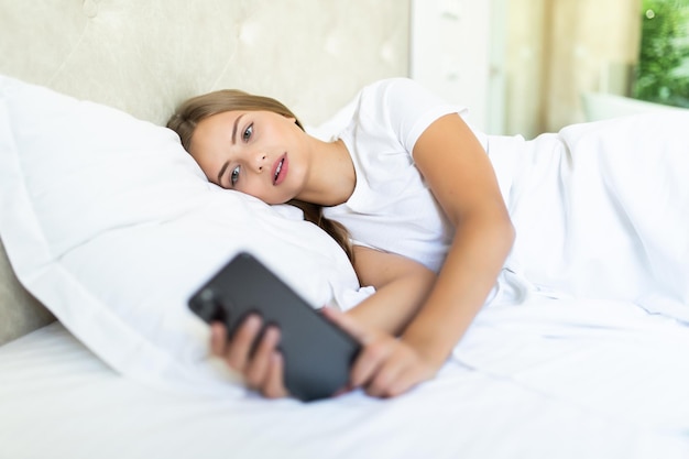 Side view of beautiful woman looking at a mobile phone while lying in bed