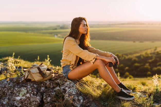 Free Photo side view of a beautiful young woman sitting on rock