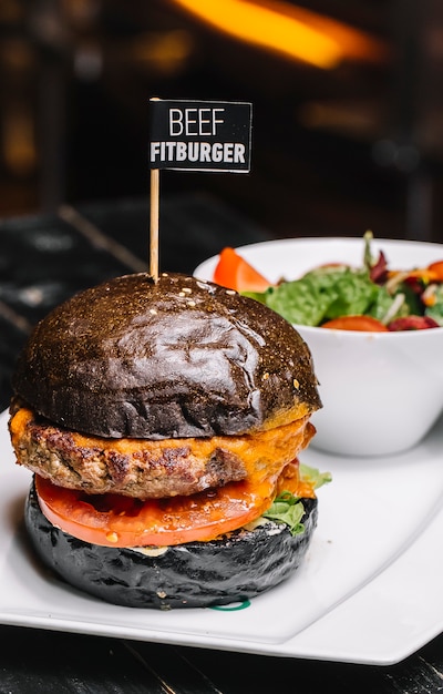 Free Photo side view beef fitburger in a black bun with vegetable salad