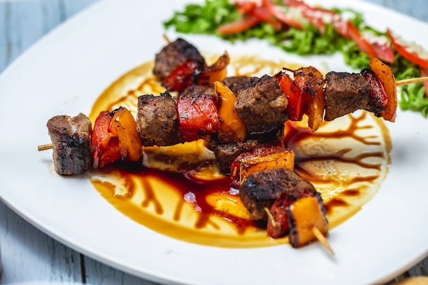 Free photo side view beef kebabs grilled beef with tomato red and yellow peppers and sauce on a plate