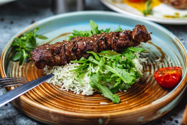 Side view beef skewers grilled beef meat with rice and arugula on a plate