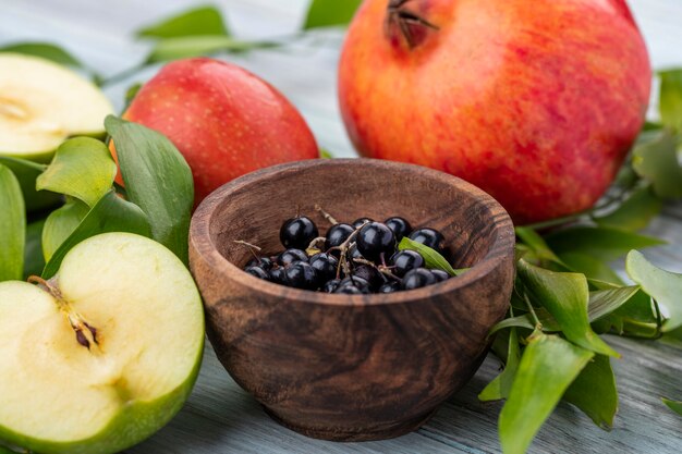 Side view of black currant in a bowl with halves of a green apple and pomegranates on a gray surface