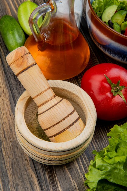 Side view of black pepper in garlic crusher with melted oil lettuce tomato cucumber salt and vegetable salad on wooden surface