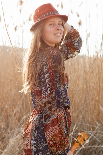 Side view of bohemian woman posing with ukulele in the field