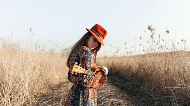 Free Photo side view of bohemian woman posing with ukulele in nature