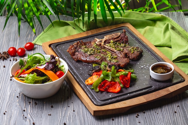 Side view bone steak with grilled vegetables and sauce on the board with vegetable salad