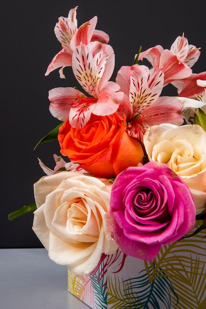 Side view of a bouquet of colorful roses and pink color alstroemeria flowers in a gift box on black table