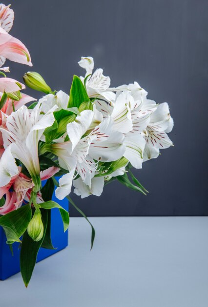 Side view of a bouquet of pink and white color alstroemeria flowers in a blue box on grey background