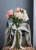 Free photo side view of a bouquet of pink and white color alstroemeria flowers in a glass vase on a wooden chair at grey wall background