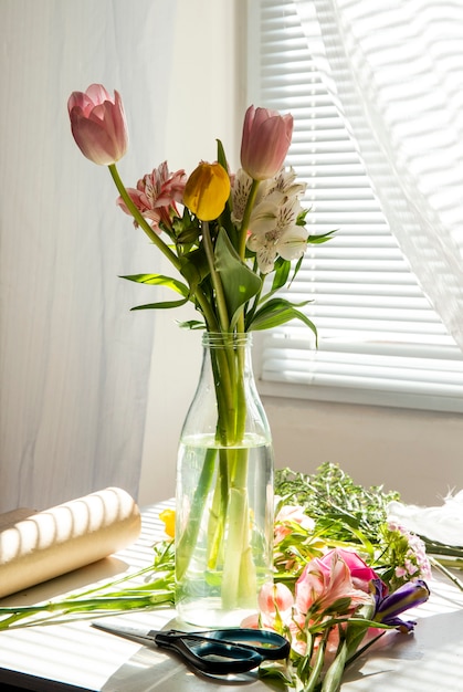 Side view of a bouquet of pink and yellow color tulips with alstroemeria flowers in a glass bottle on the table