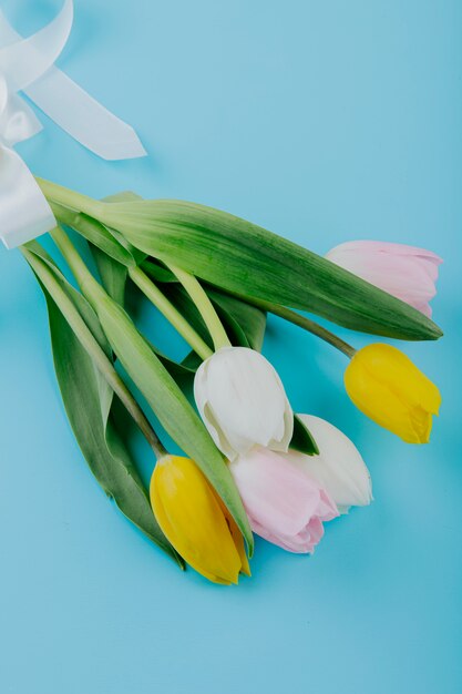 Side view of a bouquet of white yellow and pink color tulip flowers isolated on blue background