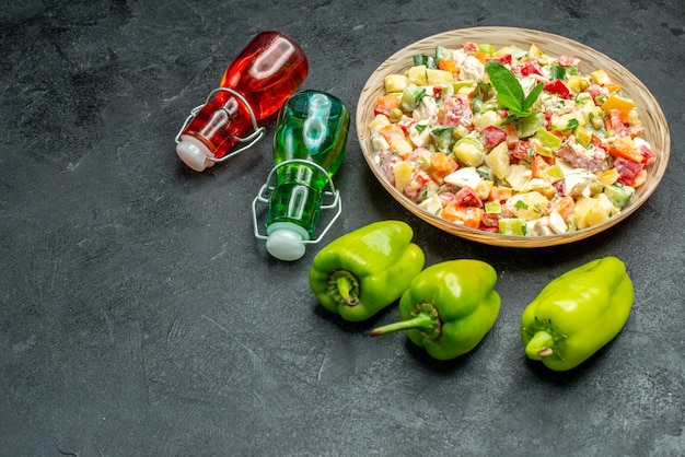 Free photo side view of bowl of vegetable salad with bell peppers and oil and vinegar bottles side on dark green table