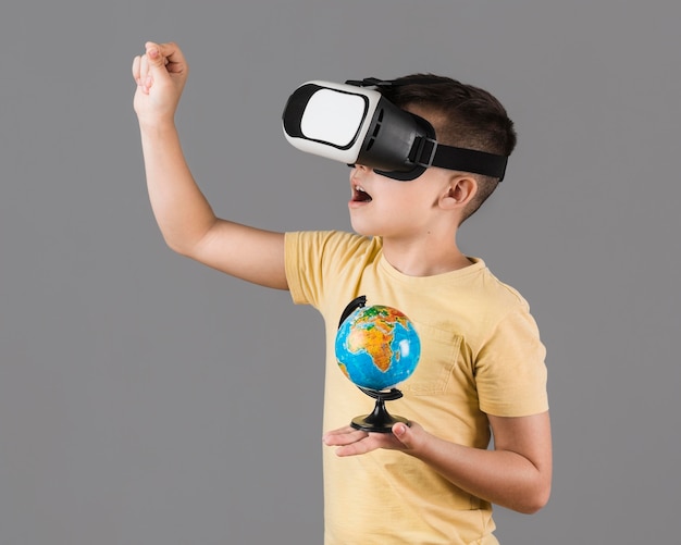 Free photo side view of boy with virtual reality headset holding globe