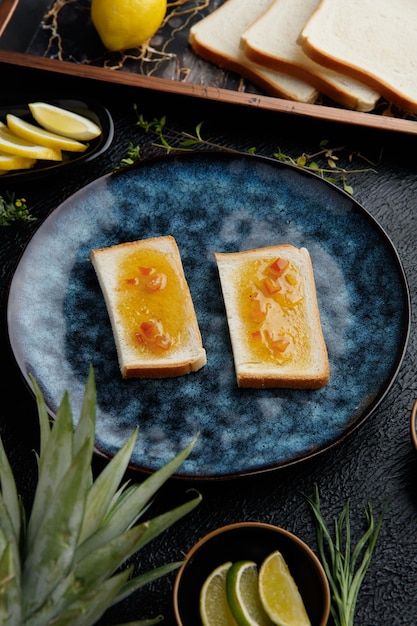 Free photo side view of bread slices smeared with jam with citrus fruits around as pineapple kiwi orange lime lemon and tangerine slices with lemon bread slices in tray on black background