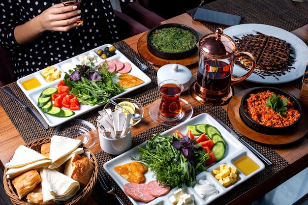 Side view of breakfast table served with various food fried eggs sausages cheese fresh salad dessert and tea