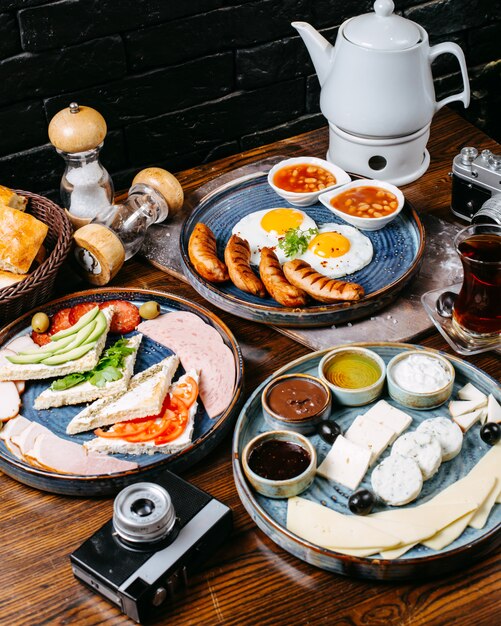 Side view of breakfast table with fried egg and sausages fresh vegetables cheese and ham