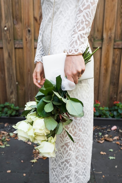 Free Photo side view of bride's hand holding white roses bouquet and clutch