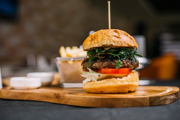 Side view of burger with beef cutlet herbs and tomato on a wooden board