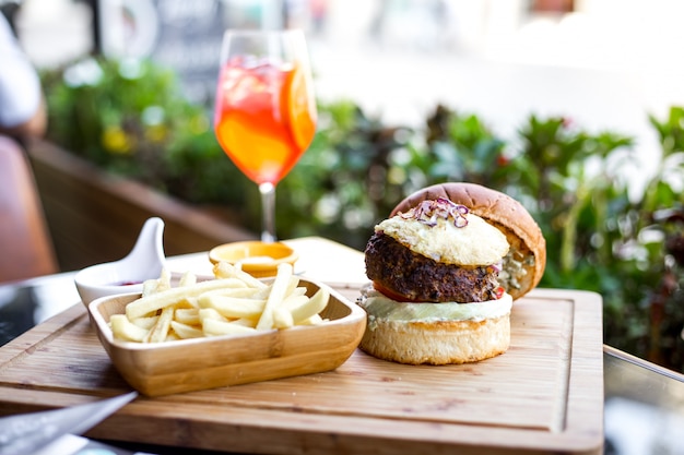 Side view burger with beef patty grilled red onion tomato lettuce in burger buns french fries and orange drink on the table