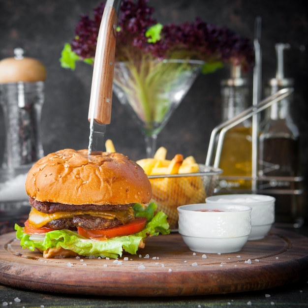 Free photo side view burger with french fries and bowl for sauce and knife in wooden food tray on restaurant