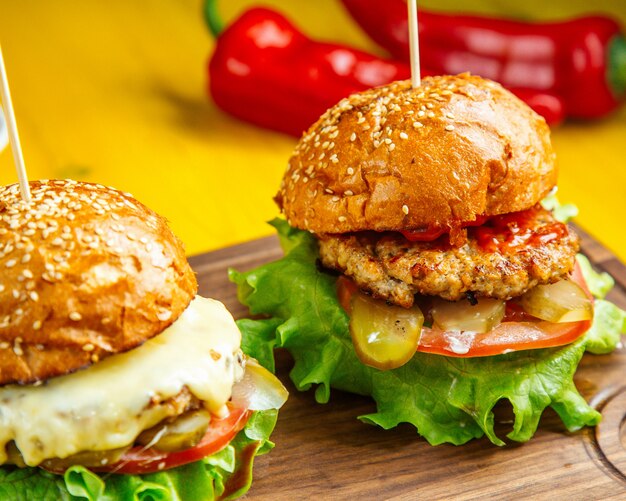 Side view of burgers with chicken cutlet melted cheese tomatoes and pickles on wooden board